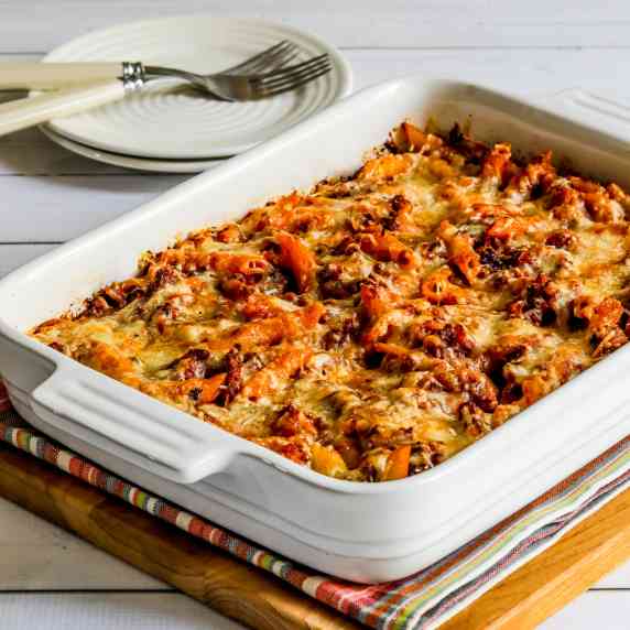 Baked Penne with Sausage shown in baking dish with plates, forks in background