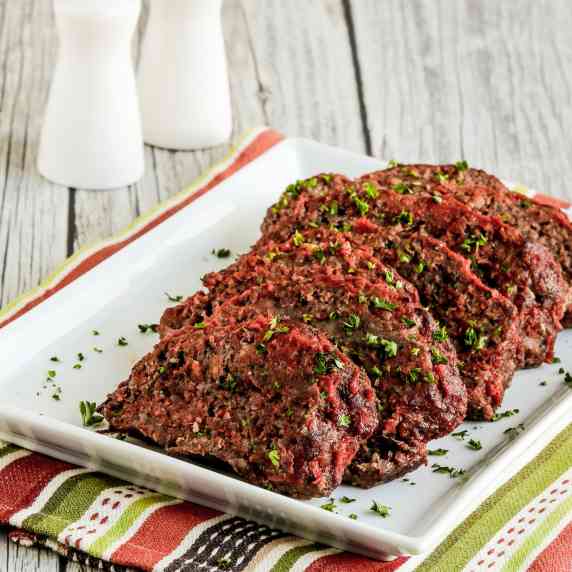 Beef and Sausage Italian Meatloaf shown on serving plate on striped napkin, with salt and pepper.