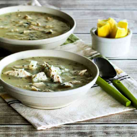 Greek Lemon CHicken Soup shown in two bowls on napkin with spoons and lemon wedges on the side.