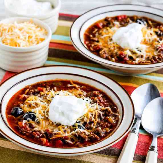 Instant Pot Ground Beef Olive Lover's Chili shown in two serving bowls with cheese and sour cream on