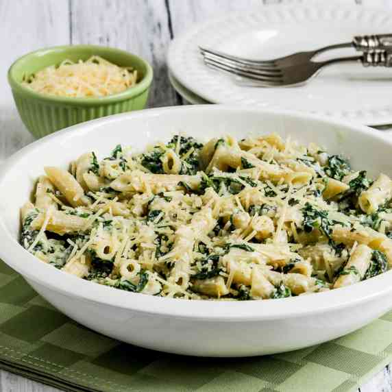 Pasta with Creamy Arugula Sauce shown in serving bowl with plates, forks, and Parmesan cheese.