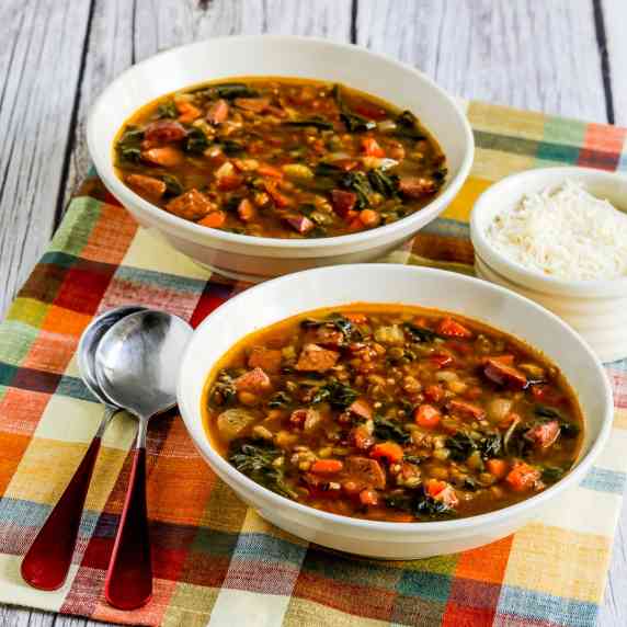 Sausage Lentil Soup with Spinach  shown in two bowls with spoons and Parmesan cheese.