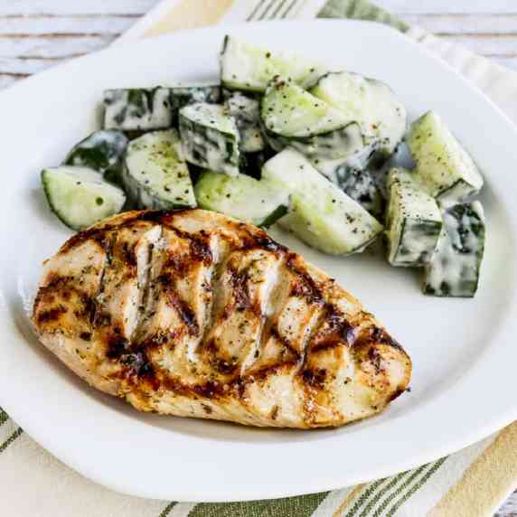 Very Greek Grilled Chicken shown on serving plate with cucumber salad.