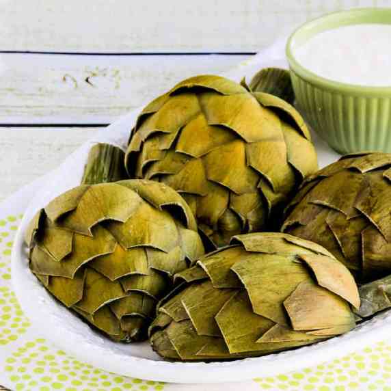 Artichokes cut in half and artichoke dipping sauce shown on serving platter.