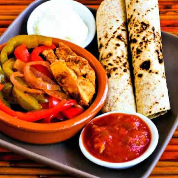 Slow Cooker Chicken Fajitas on serving plate with low-carb tortillas, salsa, and sour cream.