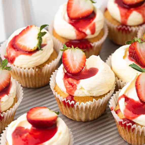 vanilla cupcakes topped with fresh whipped cream, strawberry sauce and a fresh strawberry