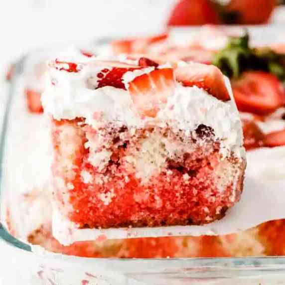 Slice of red swirled cake with strawberries being lifted from the pan.