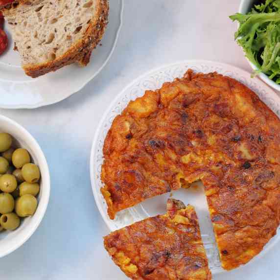 Green olives and Spanish Tortilla with chorizo in a table with greens and bread