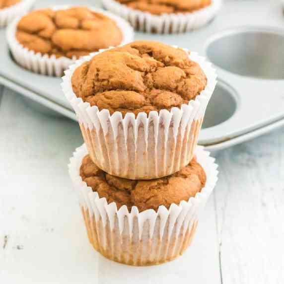 A square view of a stack of two pumpkin muffins with more muffins in a muffin tin in the background.