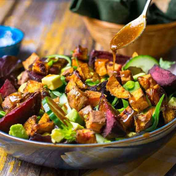A roasted beetroot and sweet potato salad being drizzled with asian-style salad dressing. 