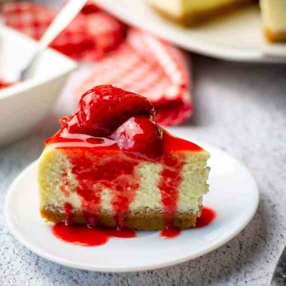 A slice of New York cheesecake with strawberry compote on top on a white plate. 
