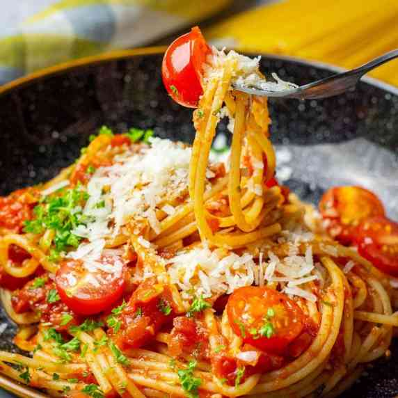 A bowlbul of spaghetti arrabbiata with cherry tomatoes, garnished with parsley. 