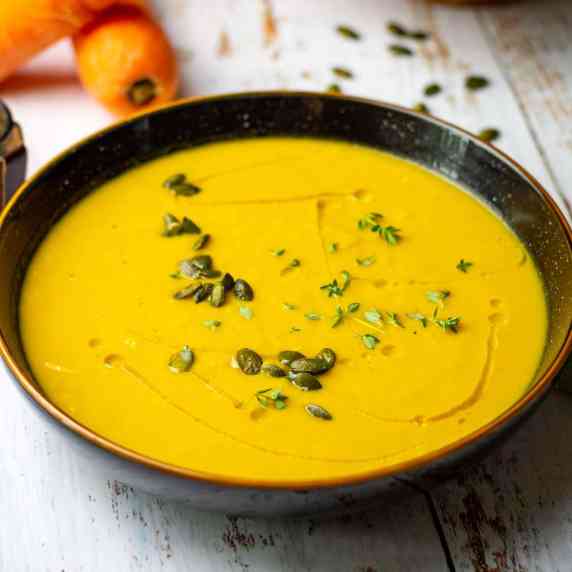 Carrot and leek soup in a black bowl with a drizzle of oil and pumpkin seeds on top.