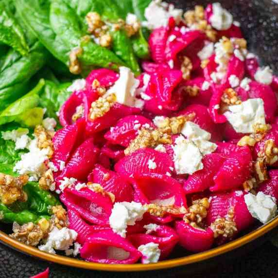 Beetroot pasta with feta adn pecans in a black bowl. 