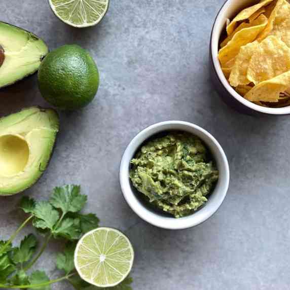 bowl of guacamole surrounded by chips, avocado, lime, and cilantro.