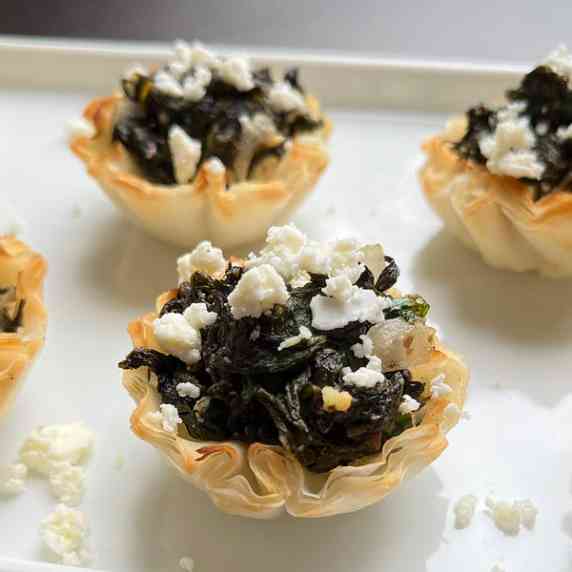 Spinach pie filling stuffed into flaky mini pastry shells and topped with feta cheese.