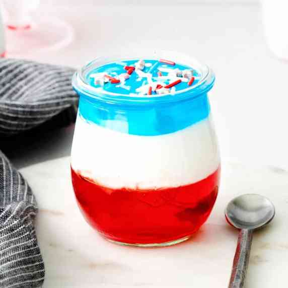 red, white, and blue layered dessert in glass jar with silver spoon next to it