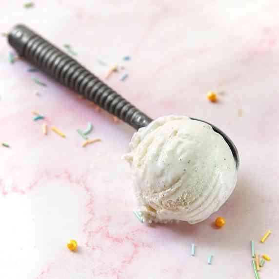 A scoop of shiitake ice cream on a pink marble surface surrounded by sprinkles.