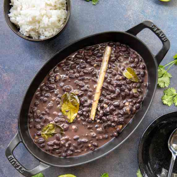 A black braiser full of black beans with whole spices in it.