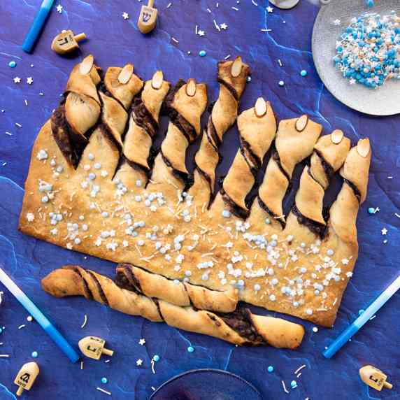 Babka bread fashioned into the shape of a menorah, surrounded by candles and dreidels. 