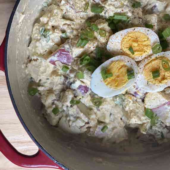 Red cast iron pan filled with potato salad with hard boiled eggs and green onions