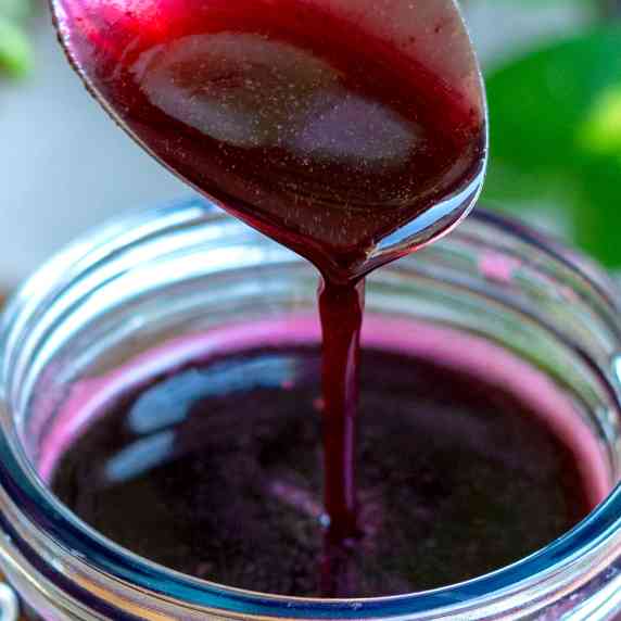 A table spoon of homemade blueberry syrup being poured into the mason jar