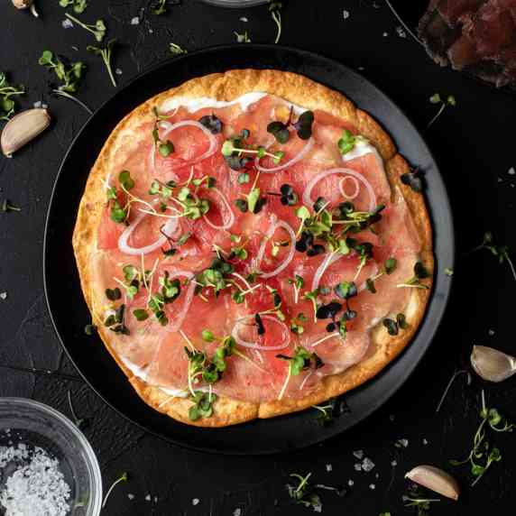 Ahi Tuna pizza over black plate centered on a black background. 