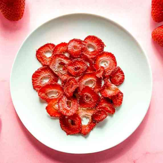 Dehydrated strawberry slices on a white plate on a pink background.