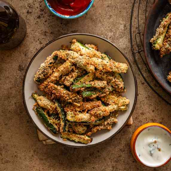 crispy air fryer zucchini fries are served in a round beige plate with a white creamy dip