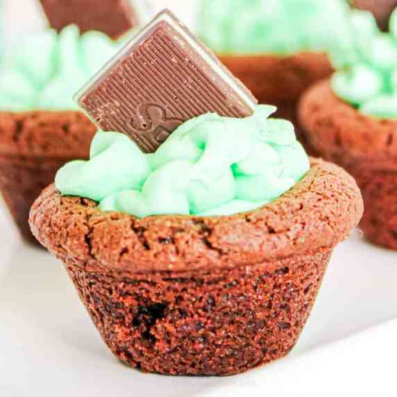 Close up of a chocolate cookie cup filled with frosting & a chocolate mint candy on a serving tray.