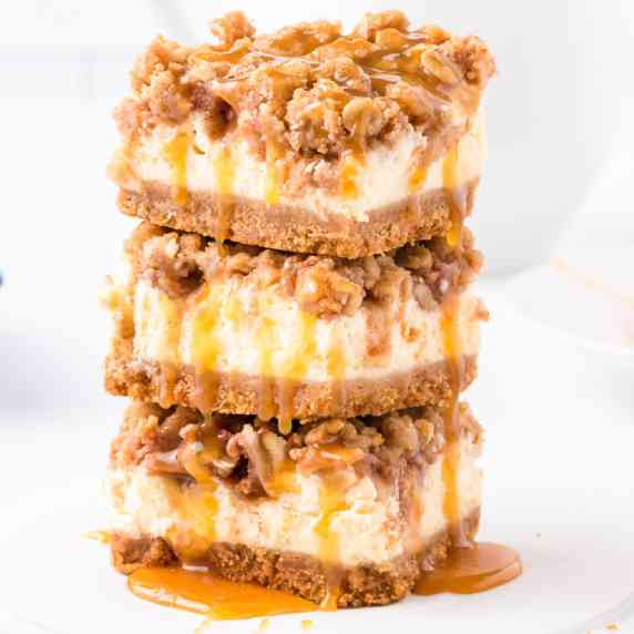 Three stacked apple caramel cheesecake bars with lots of gooey caramel from the side.