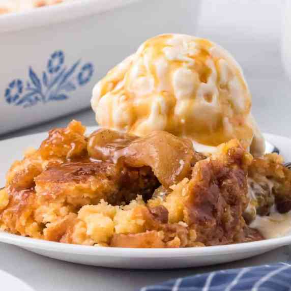 Caramel apple dump cake on a plate topped with ice cream and more caramel on a plate.