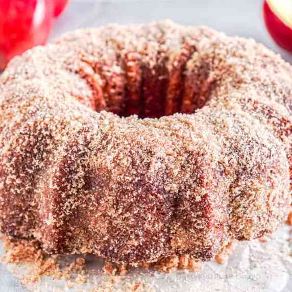 Side view of an apple cider doughnut cake covered in cinnamon sugar.