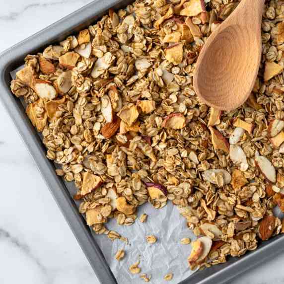 Apple Cinnamon Granola on a baking sheet with a wooden spoon.