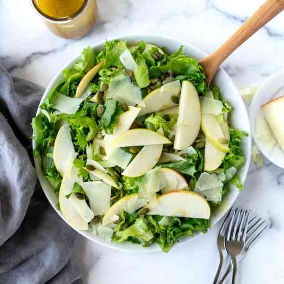 Apple Manchego Salad in a white serving bowl with a wooden spoon.
