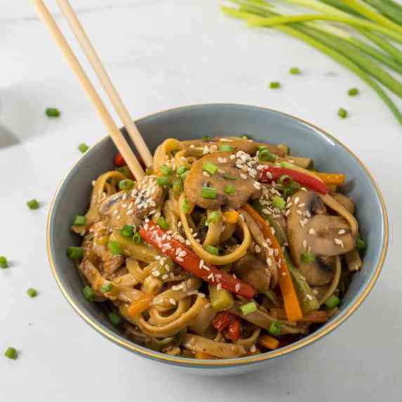 A bowl of Asian-style vegetable pasta with chopsticks stuck in.