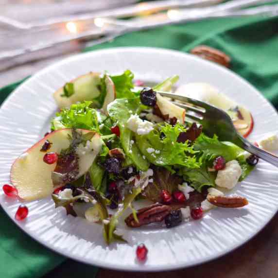 Apple Pomegranate Green Salad with Cider Vinaigrette  on a white plate on green napkin