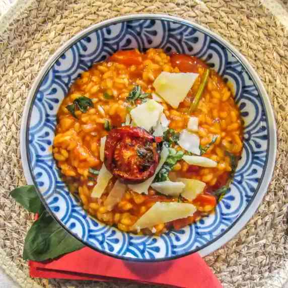 Creamy Summer Tomato Risotto served with garnishes: parmesan, roasted tomato and basil