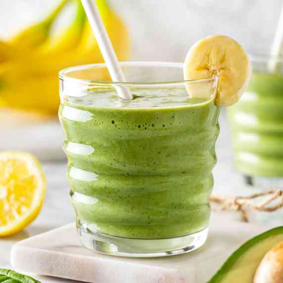 Glass with green avocado banana peanut butter smoothie decorated with a slice of banana