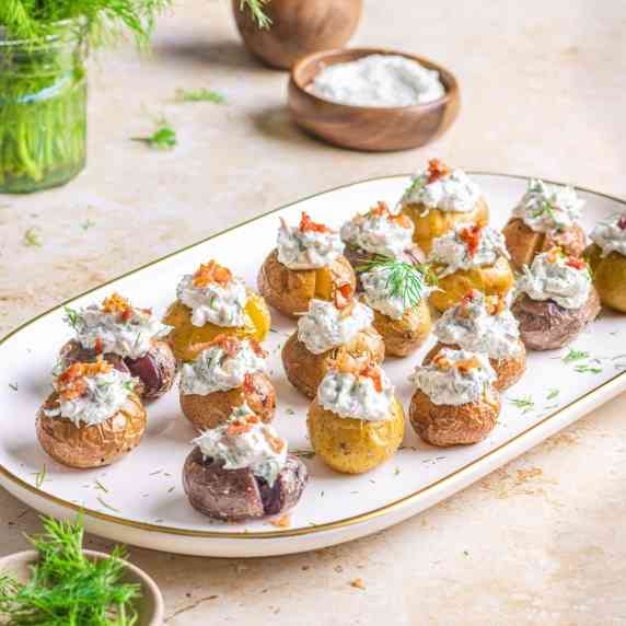 Mini potatoes with dill cream on a white platter.
