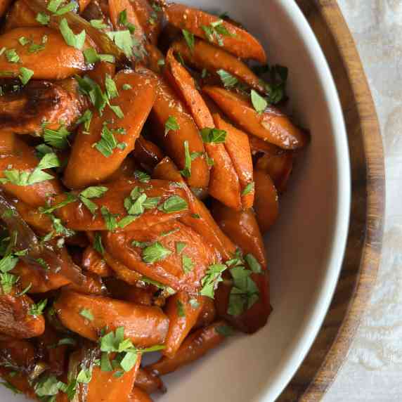 Roasted carrots and shallots garnished with fresh parsley in a white bowl.