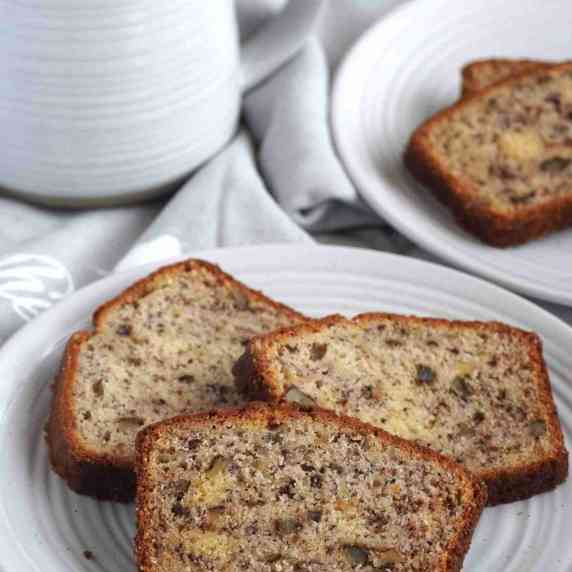 A plate of sliced banana bread with a coffee mug in the background.