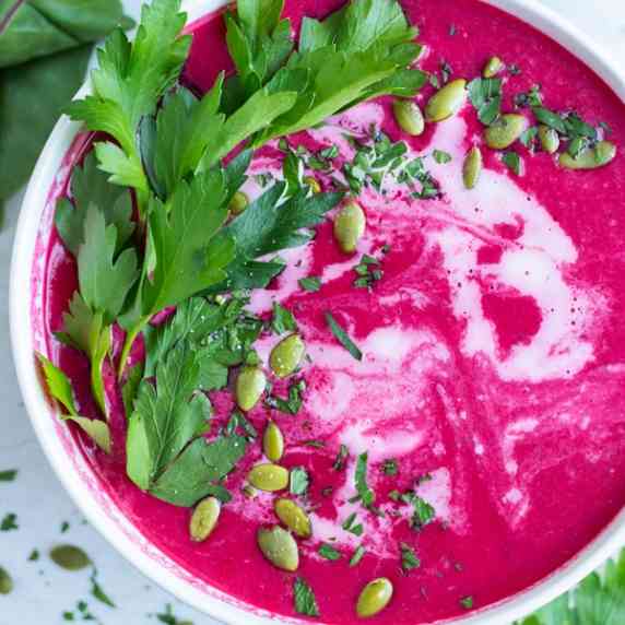 Creamy Beet Soup RECIPE in a white bowl at an overhead angle with garnishes like greens and seeds.