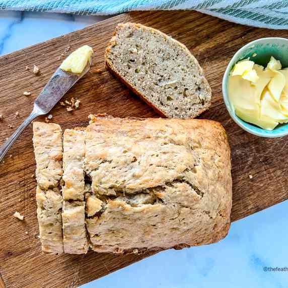 Sliced Banana Bread with a bowl of butter and bread knife on a serving board with dish towel