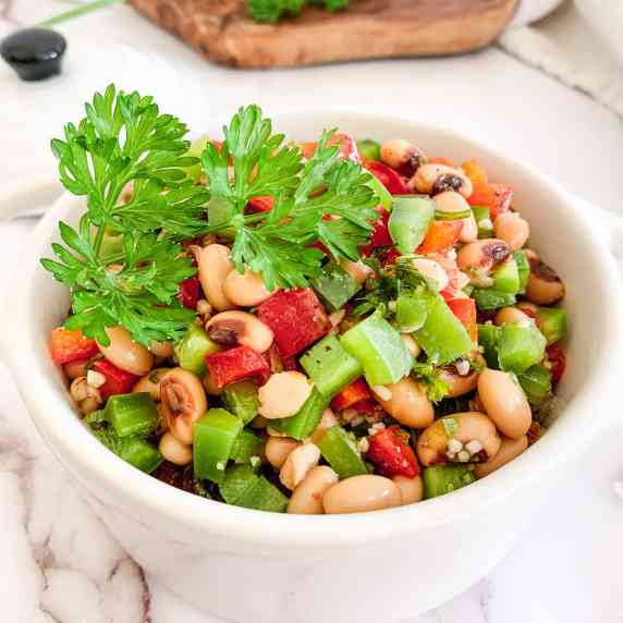 black eyed pea salad in a white pot with handles on an olive wood board with a white dish towel