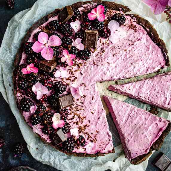 Blackberry tart with chocolate and flowers on a dark blue background. 