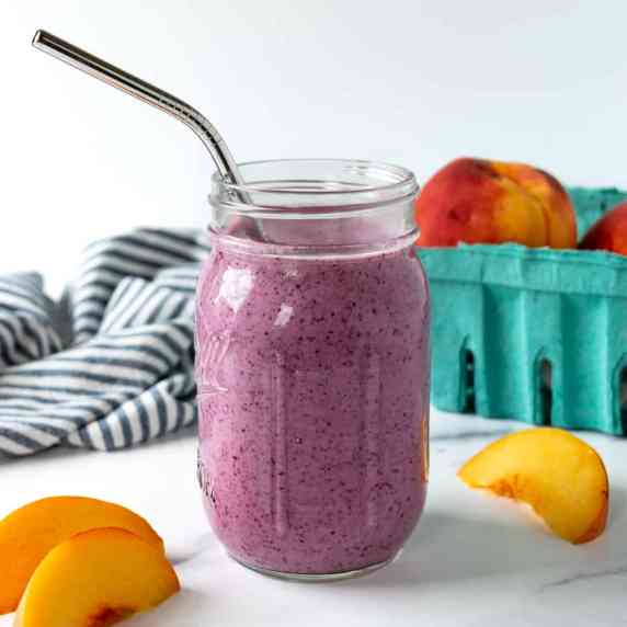 Blueberry Peach Smoothie in a mason jar with a metal straw.