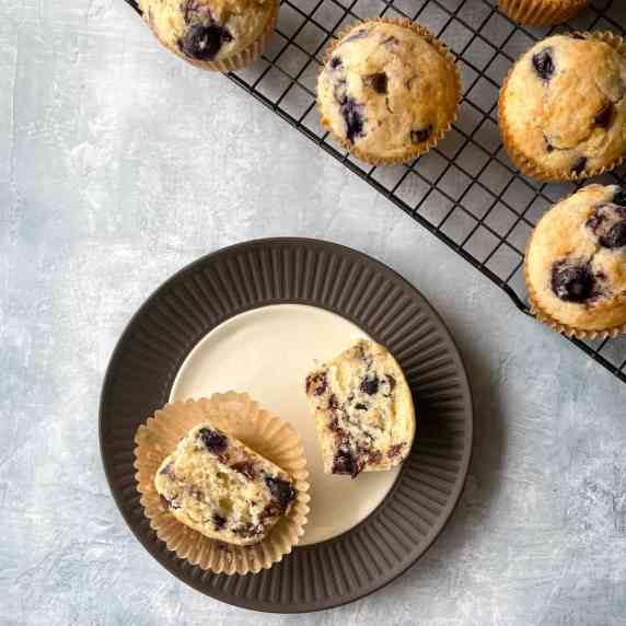 split blueberry chocolate chip muffin on a plate next to more muffins on a cooling rack.