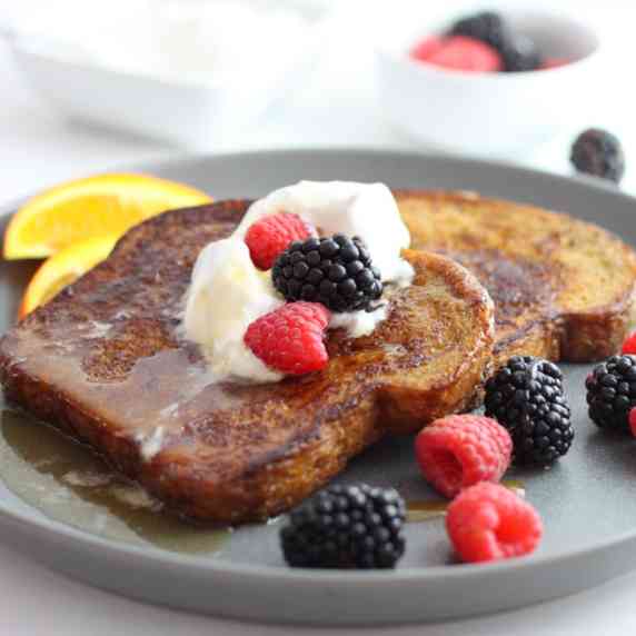 A gray plate with brown sugar french toast, berries, maple and whipped cream.