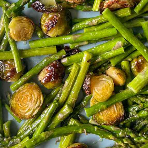 A closeup is shown of roasted Brussels sprouts and asparagus on a blue sheet tray.